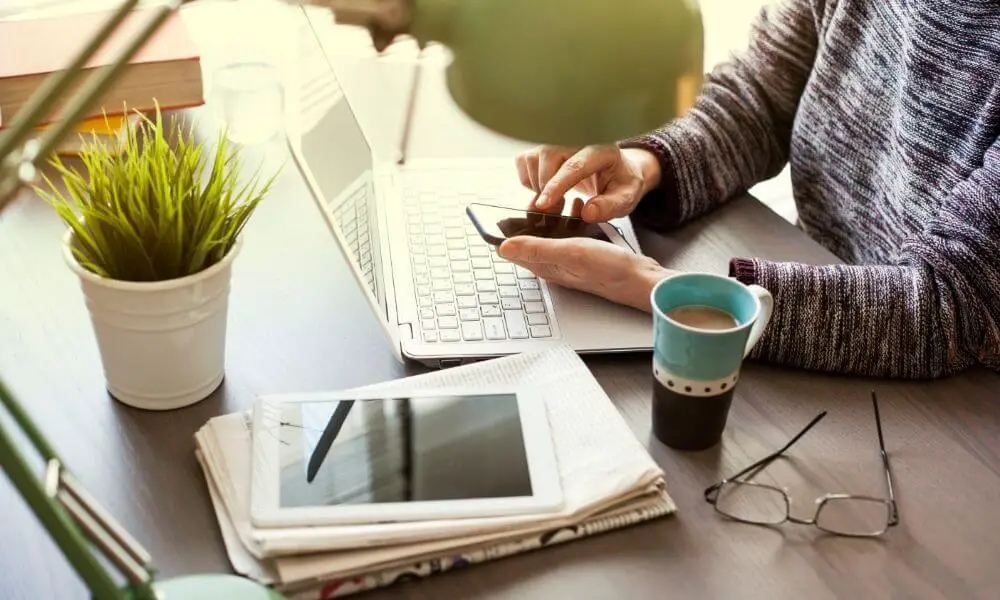 person at computer with coffee and electronics