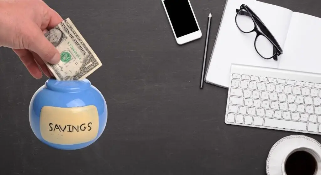 cash going into a savings jar sitting on a desk