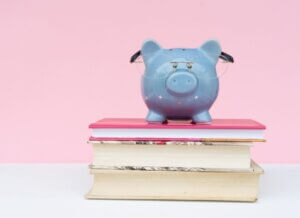 blue piggy bank with glasses sitting on books